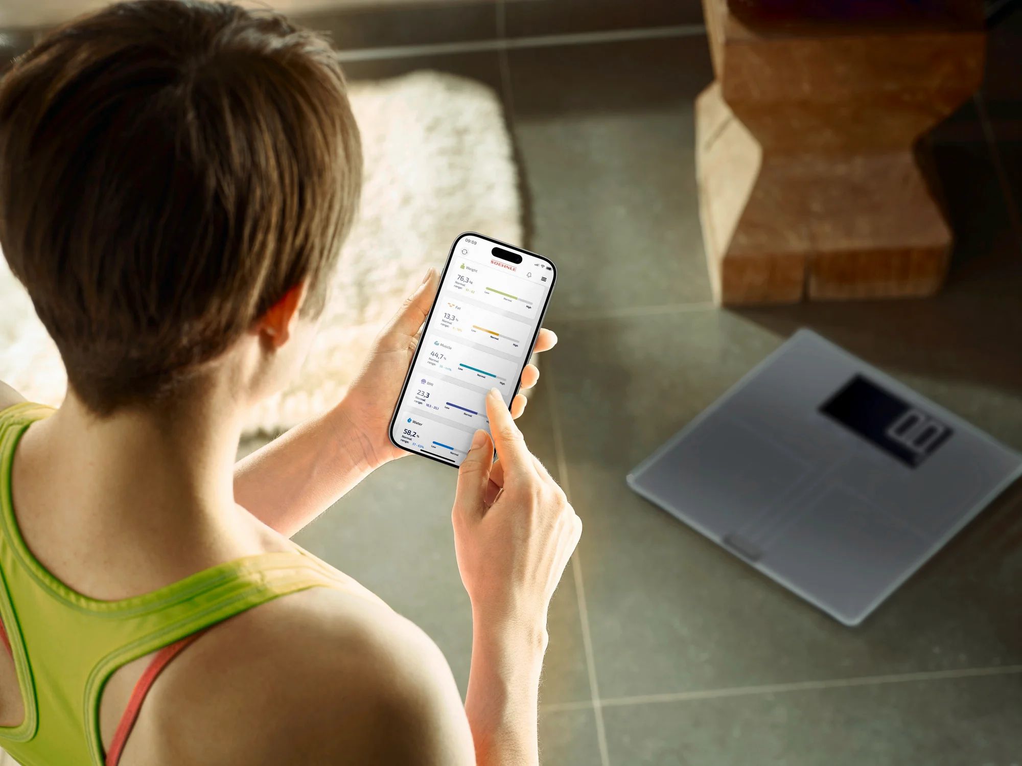 Donna con smartphone vicino alla bilancia. Bilancia grigia con display digitale. Lo smartphone mostra grafici.