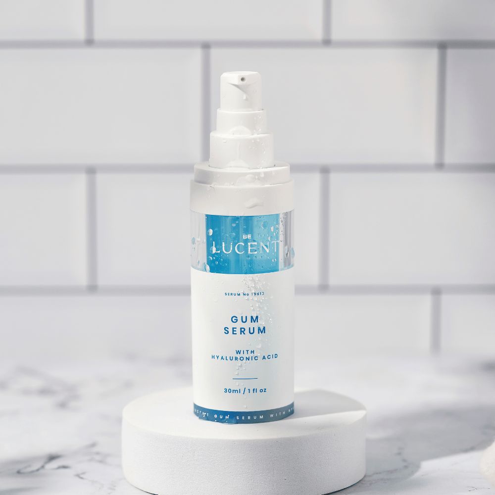 Flacone di siero gengivale su piedistallo. Bianco e blu. Scritta: GUM SERUM, Be Lucent. Con acido ialuronico. 30ml/1 fl oz.