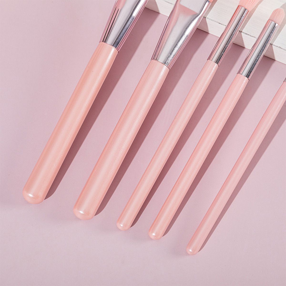 Primo piano di manici e setole di pennelli per il trucco rosa con ghiere argentate.