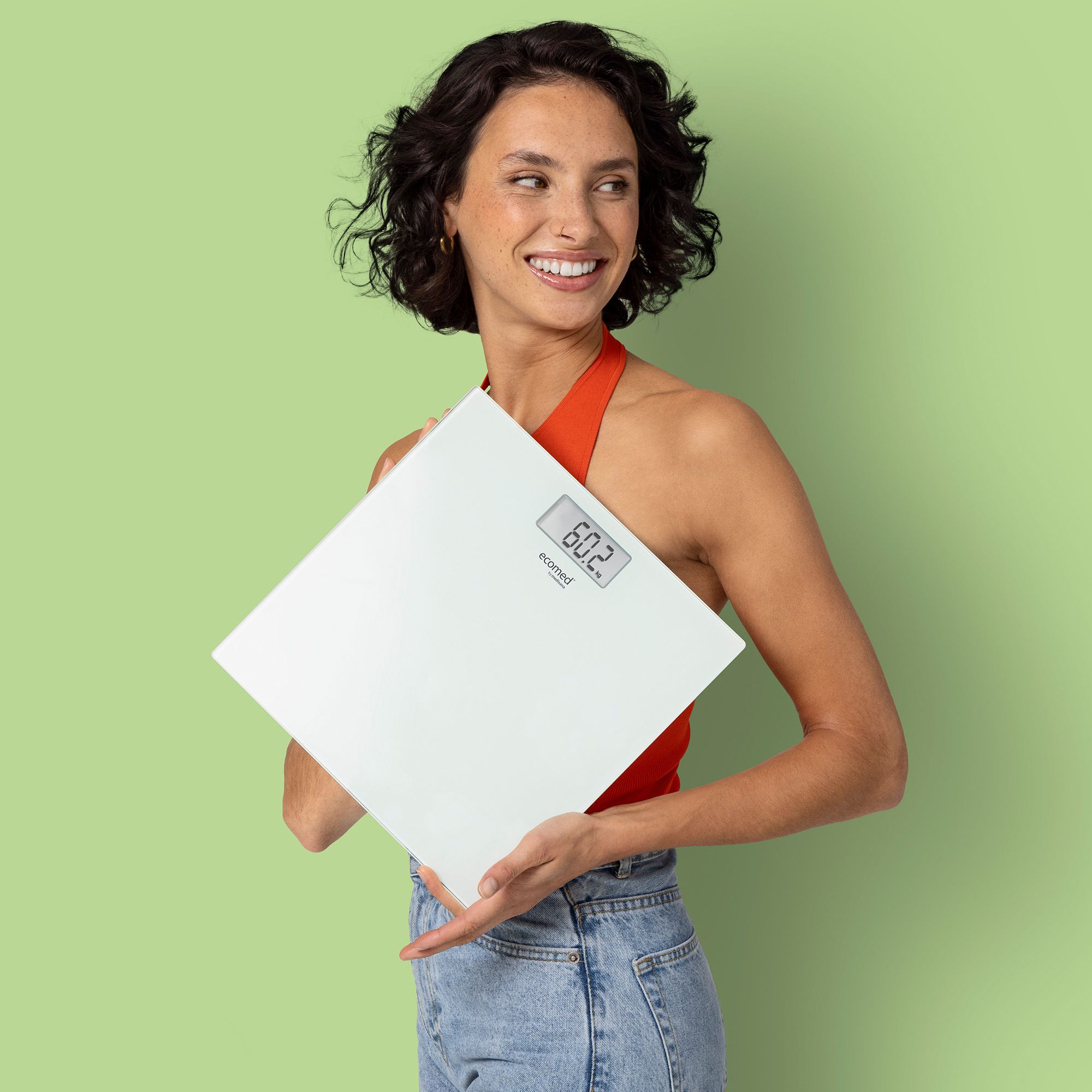 Una donna tiene una bilancia pesapersone bianca in vetro con display digitale (60.2 kg).