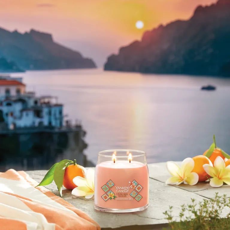 Yankee Candle Capri Glow. Candela rosa a due stoppini. Adesivo con motivi floreali. Sfondo: mare, montagne, tramonto.