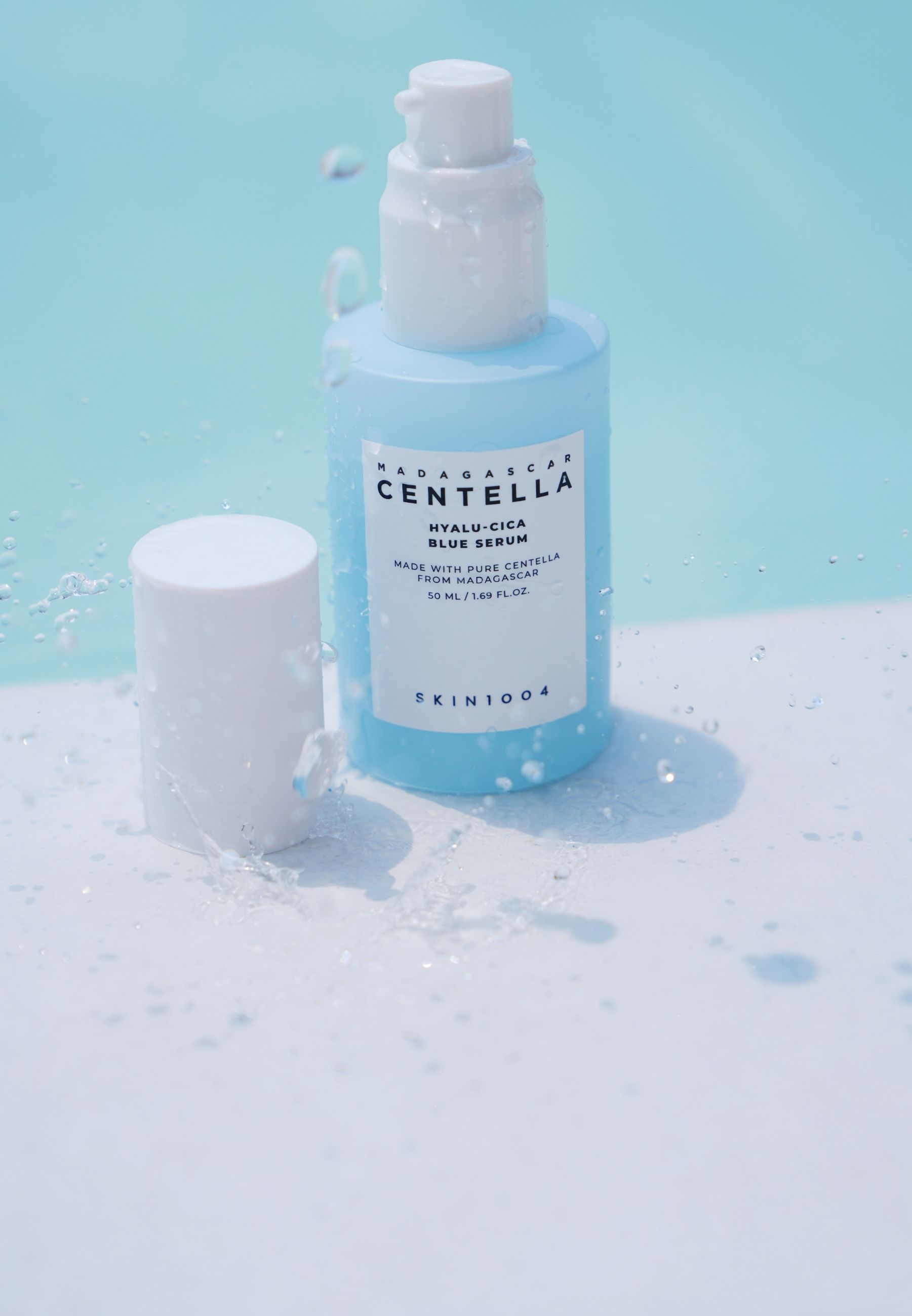 Flacone di siero con spruzzi. Scritta: MADAGASCAR CENTELLA HYALU-CICA BLUE SERUM. Marchio: SKIN1004. Flacone e tappo.