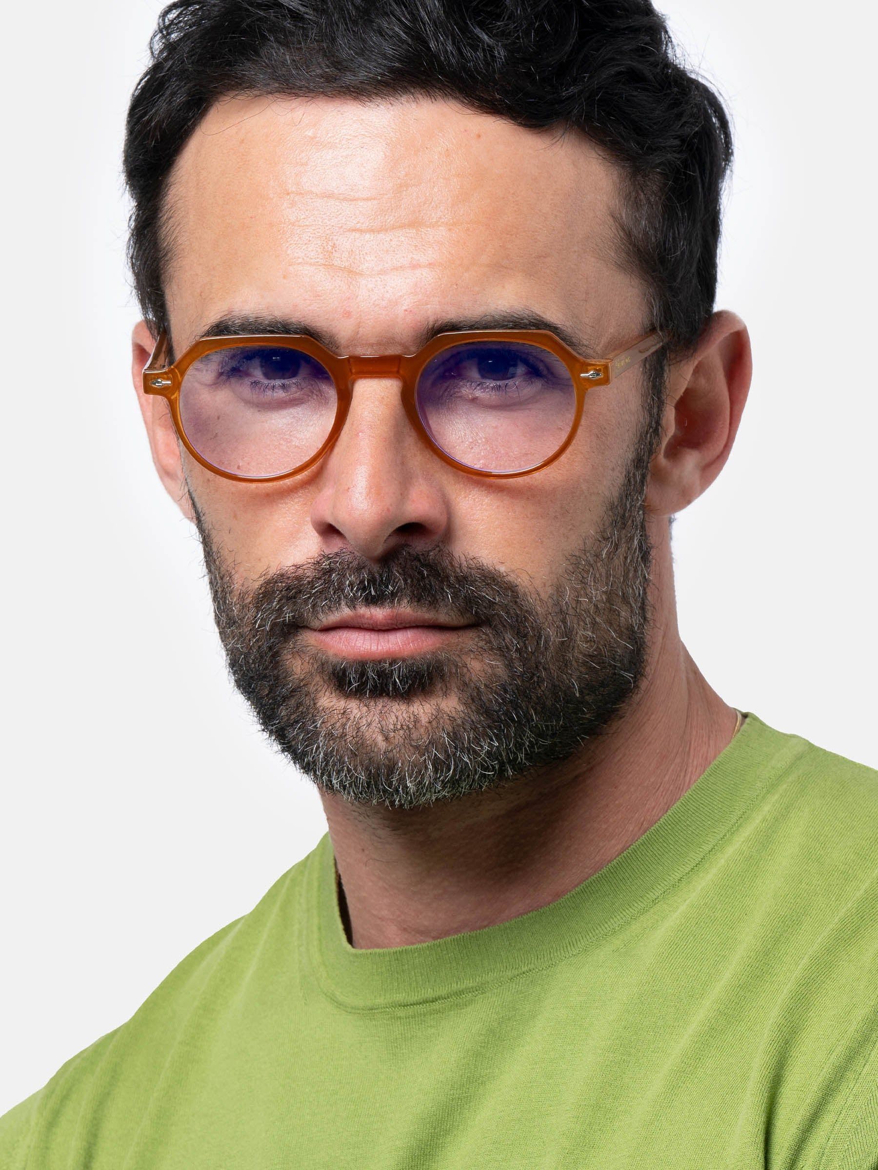 Uomo con occhiali marroni con lenti rotonde. Gli occhiali sono indossati. L'uomo indossa una maglietta verde.