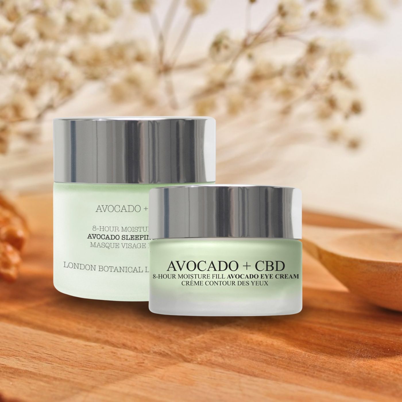 Due vasetti di vetro con coperchi argentati. Testo: Avocado + CBD, Avocado Sleeping Mask e Eye Cream. Su sfondo legno.