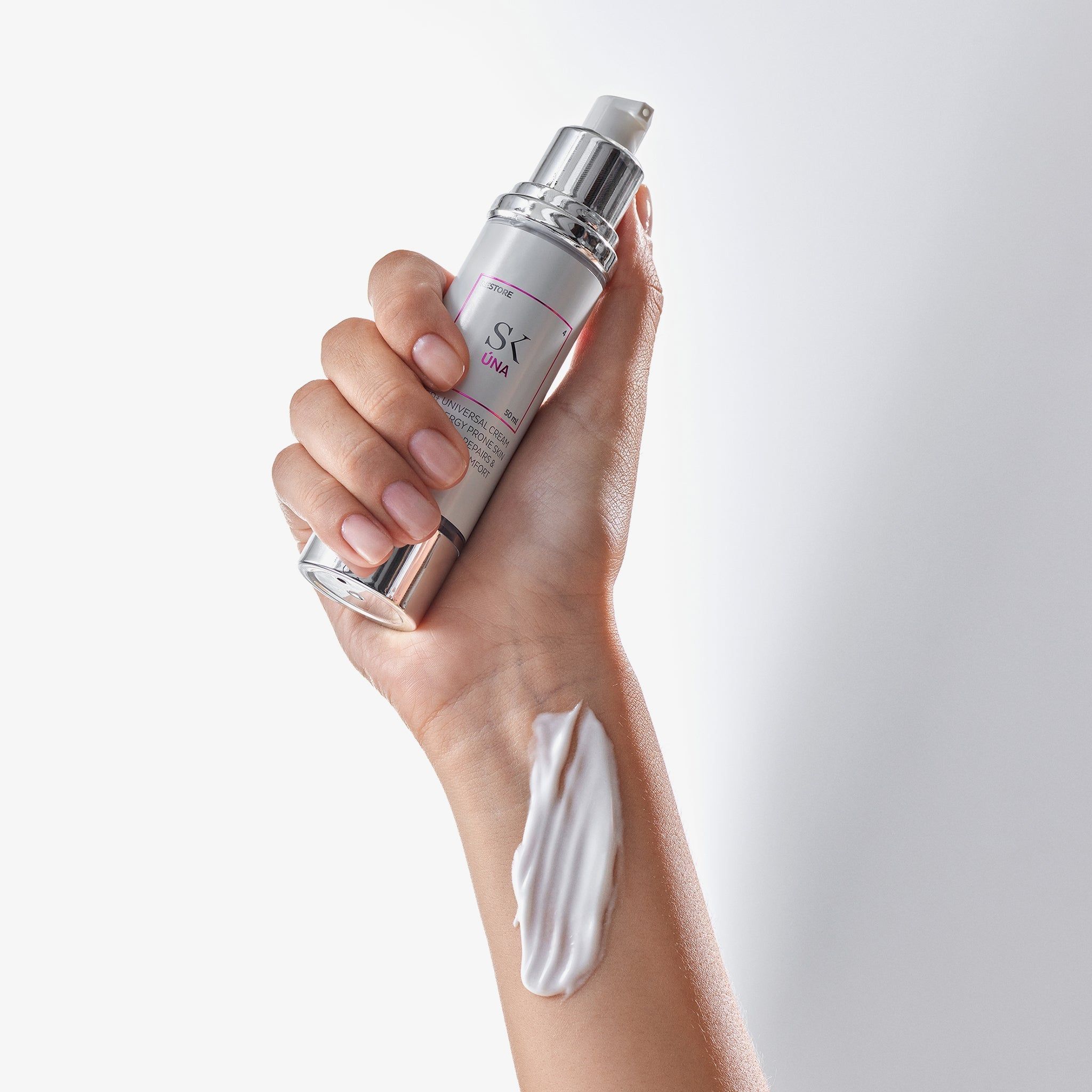 Mano che tiene un dispenser di crema. Crema sul dorso della mano. Testo: SK Úna, MED+ UNIVERSAL CREAM, per pelli allergiche.