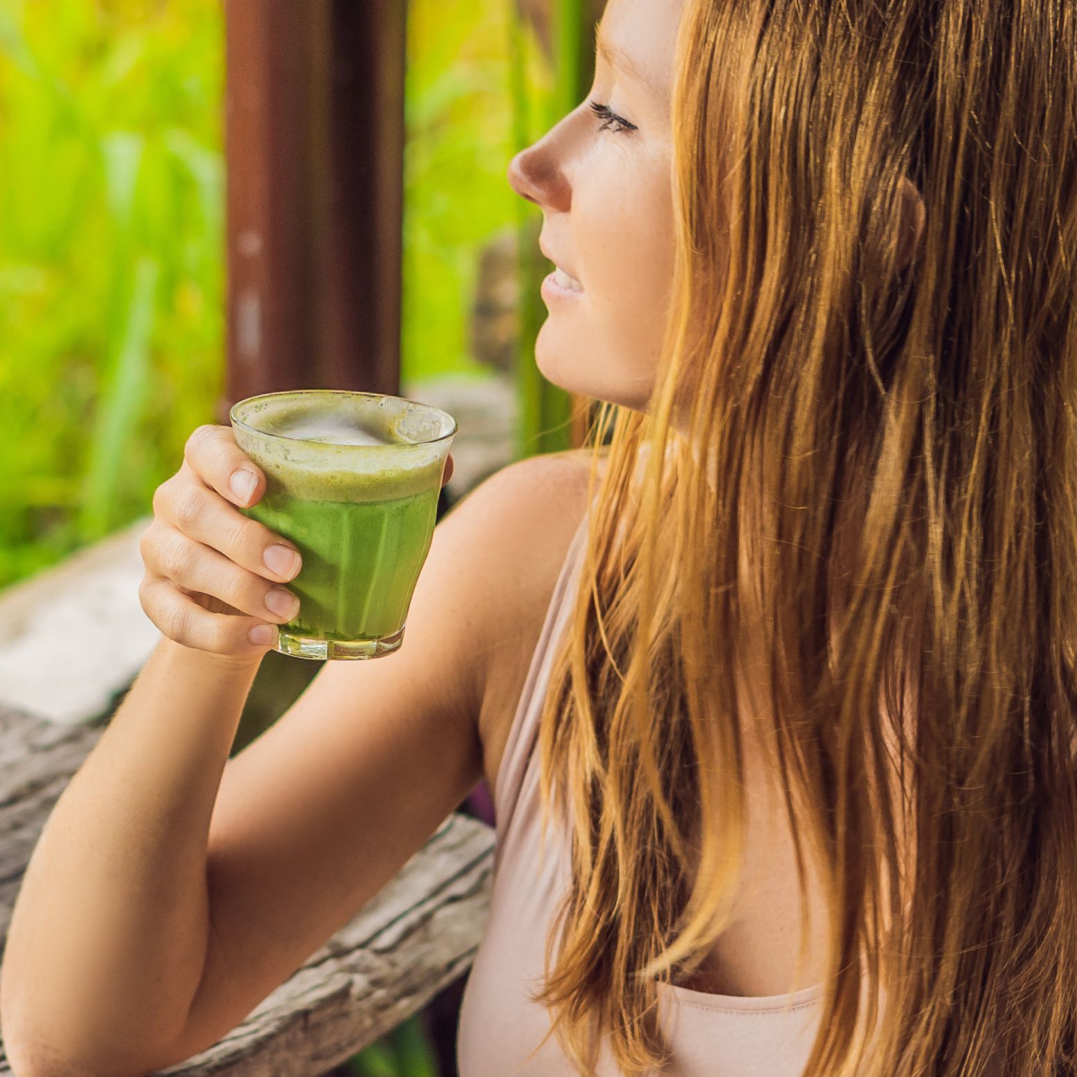 Una donna tiene in mano un bicchiere di tè matcha. Il tè è verde e in un bicchiere. La donna è vista di profilo.