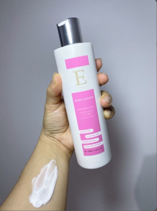 Bottiglia bianca con etichetta rosa. Tappo argentato. Mano che tiene la bottiglia e crema sul braccio. Testo: Body Lotion, Acido Ialuronico + Collagene, Aloe Vera, Melograno.