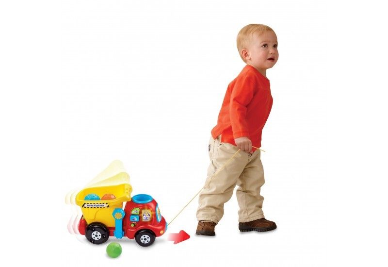 Autocarro ribaltabile giallo e rosso con corda. Un bambino tira il camion. Palla verde a terra.