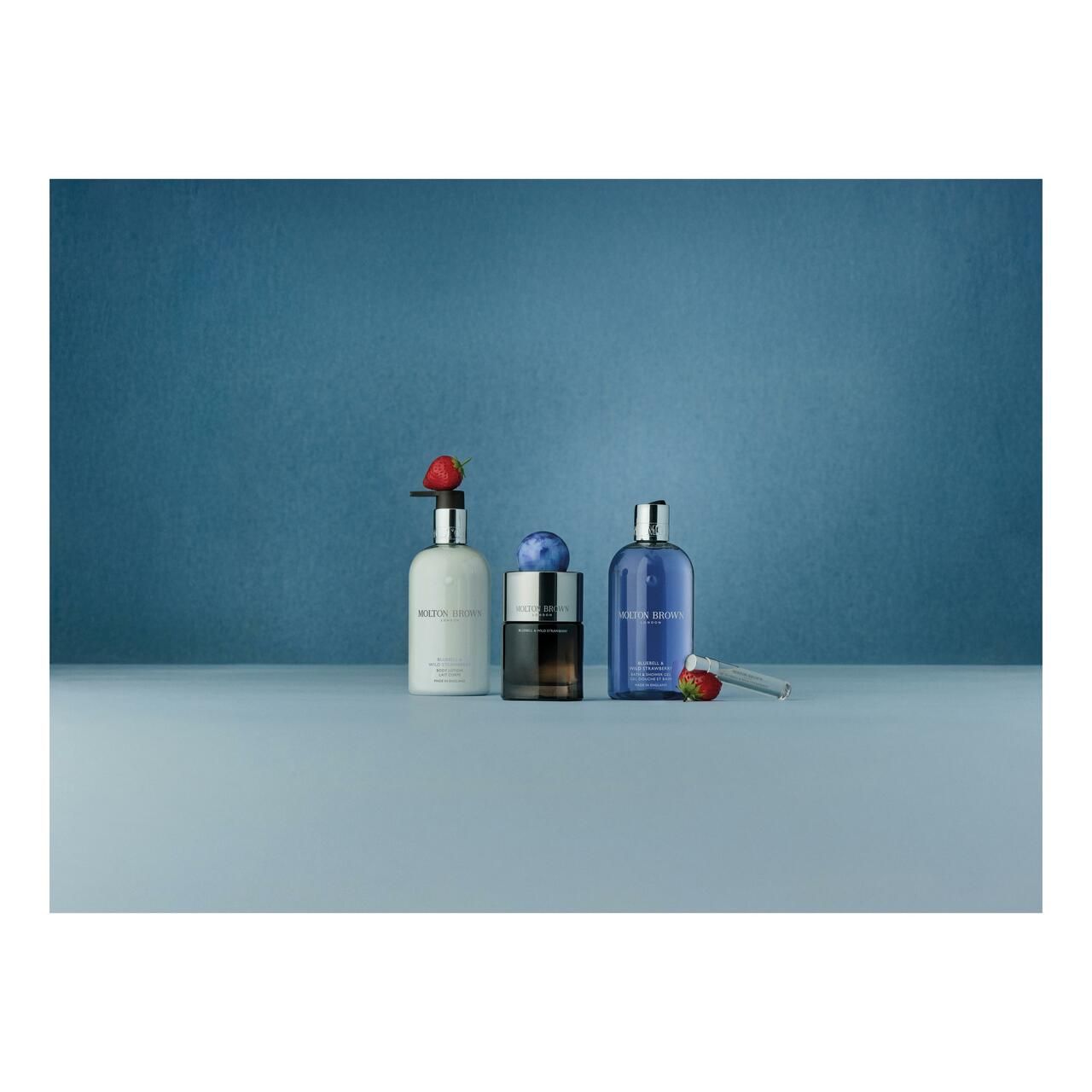 Tre flaconi su sfondo blu. Due con scritta bianca, uno con tappo blu. Fragole.