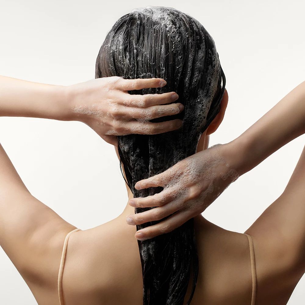 Persona che si lava i capelli con shampoo. Mani sulla nuca. Capelli neri coperti di schiuma.