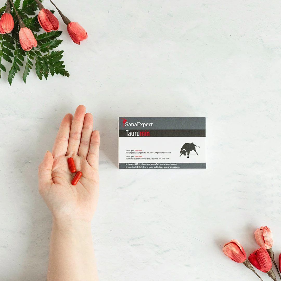 Mano con capsule rosse e scatola SanaExpert Taurumin.