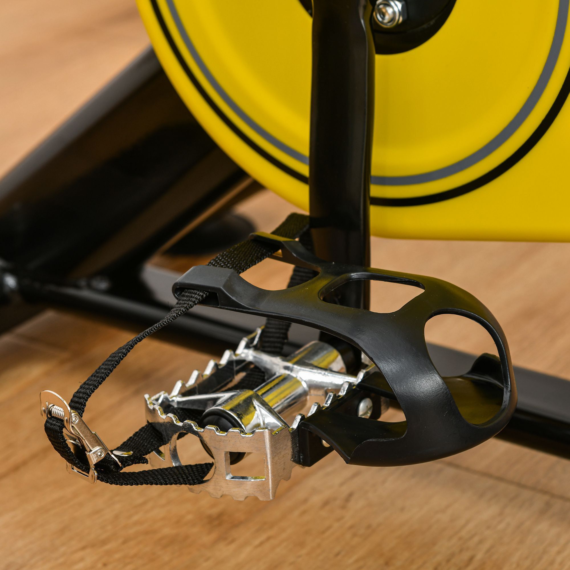 Pedale della bici con cinturino nero. Plastica nera, metallo argentato. Ruota gialla sullo sfondo.