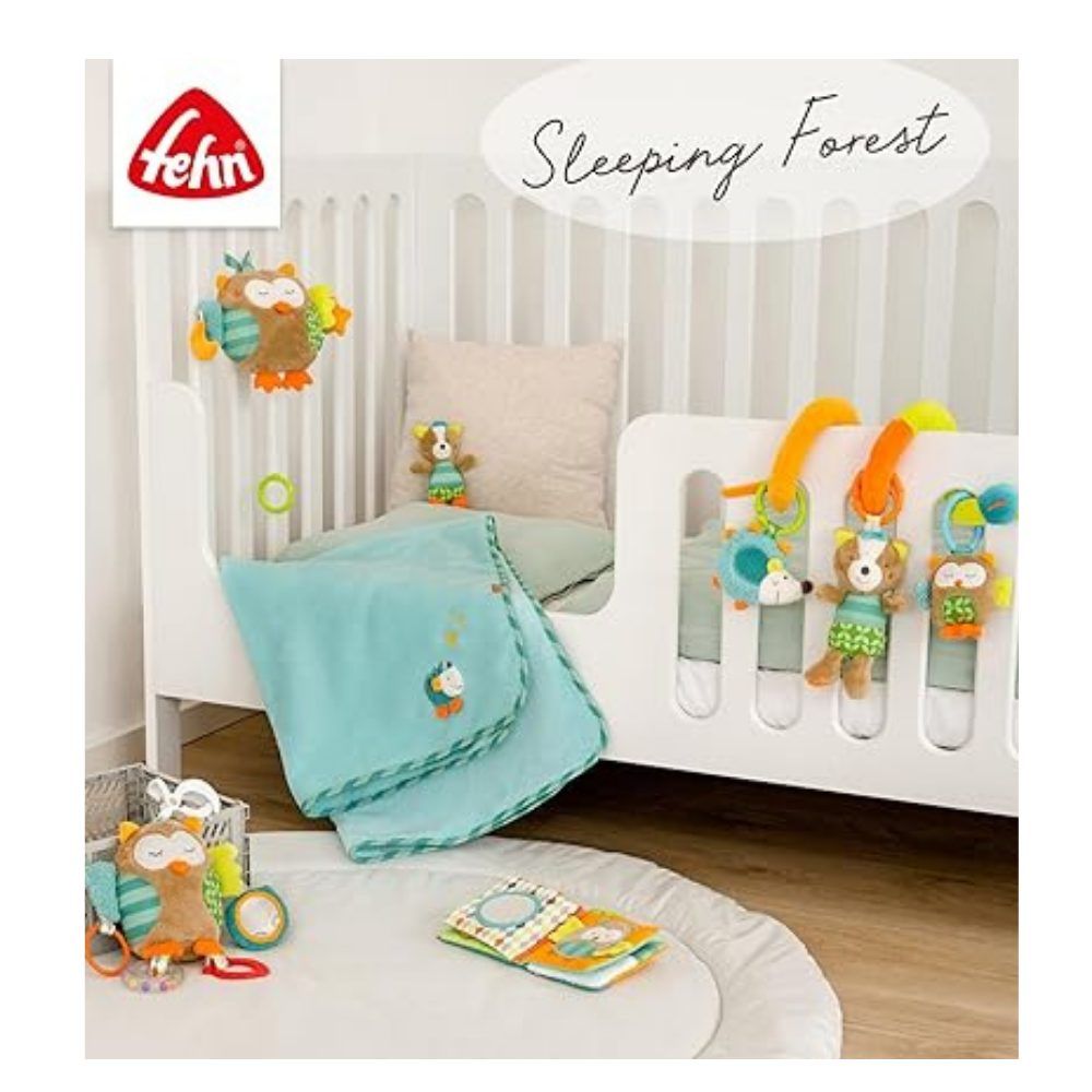 Set di giocattoli per bambini con libro in tessuto e peluche. Marchio: fehn. Su un lettino bianco. In sottofondo: giocattoli e decorazioni.