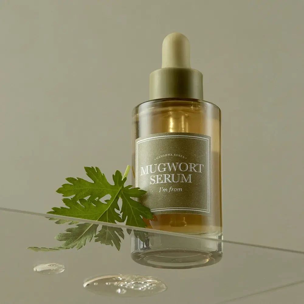 Flacone di vetro con siero "Mugwort Serum". Foglia verde accanto. Gocce su superficie vetrata.