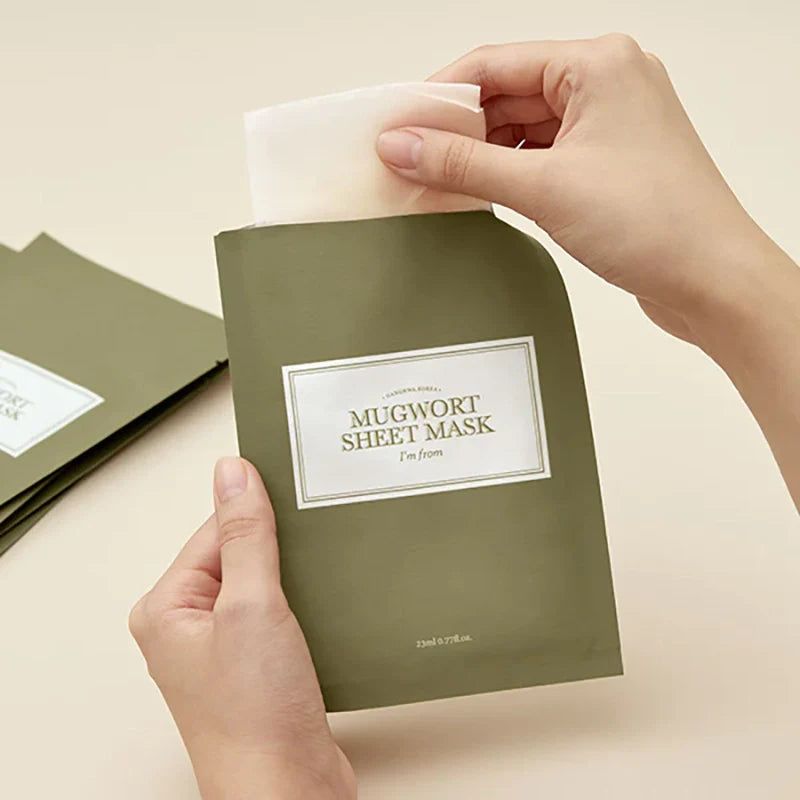 Mani che aprono una confezione verde con la scritta 'Mugwort Sheet Mask'.