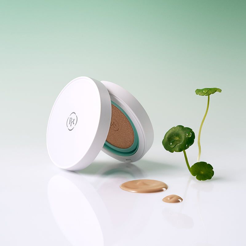 Contenitore compatto cushion aperto, accanto macchie di prodotto e pianta. Bordo verde visibile.