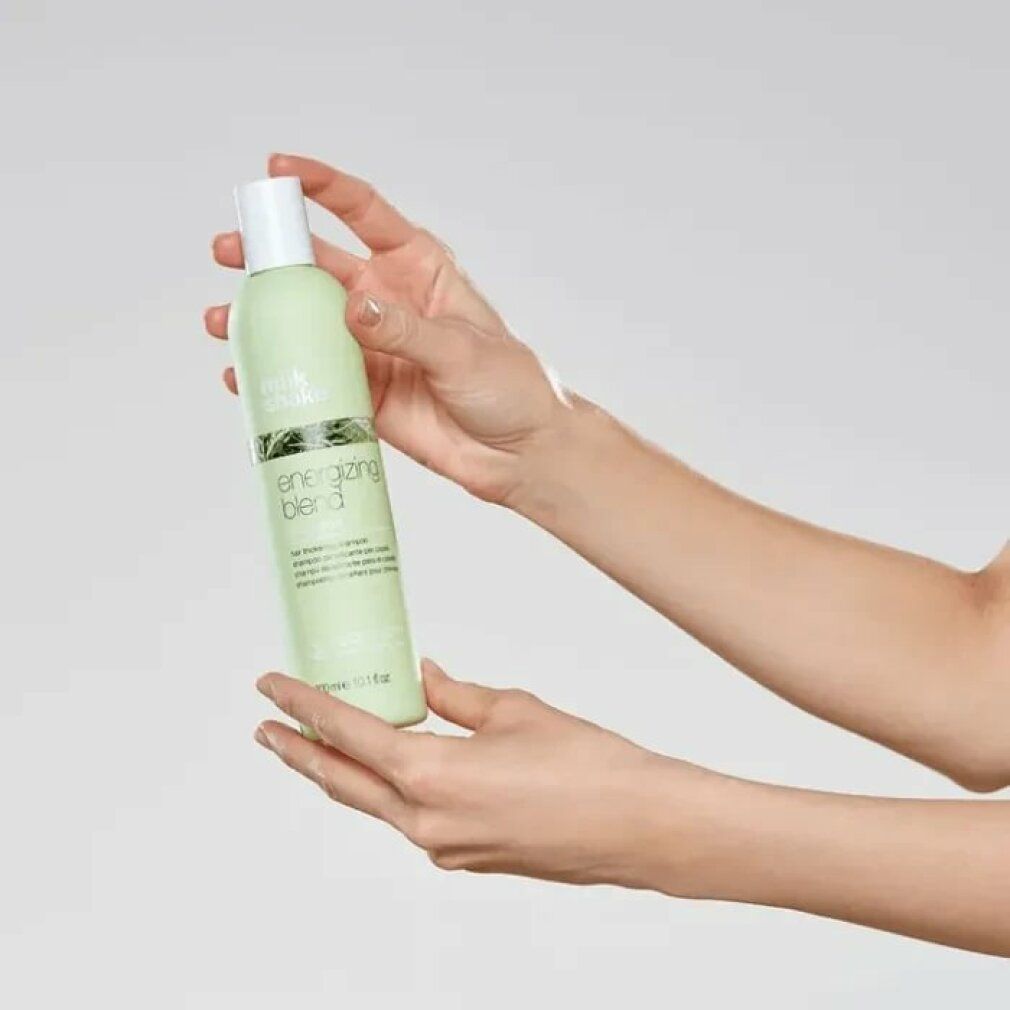 Flacone di shampoo verde chiaro con tappo bianco. Scritta: energizing blend shampoo. Tenuto in mano.