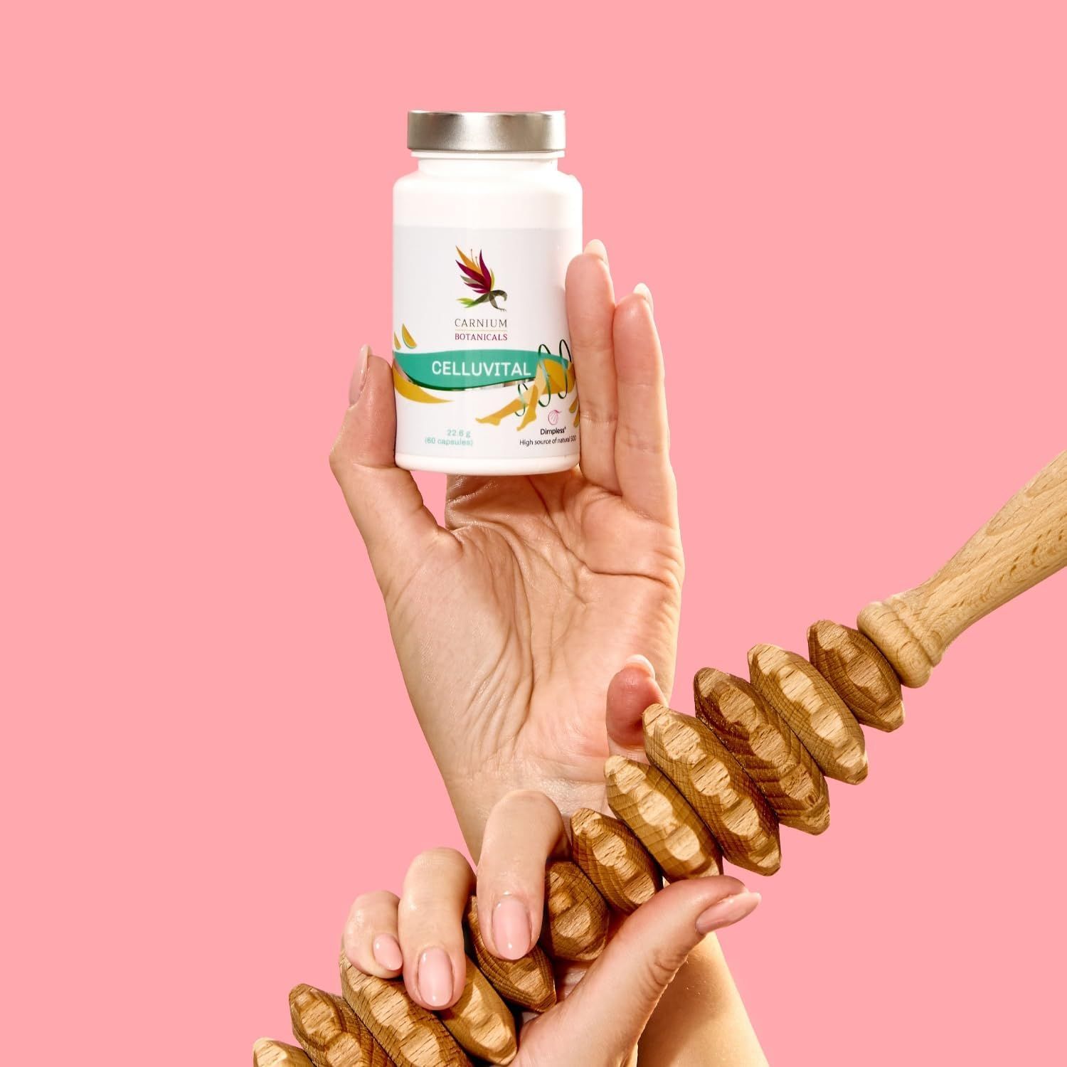 Mano che tiene un flacone CELLUVITAL e un massaggiatore. Sfondo rosa.
