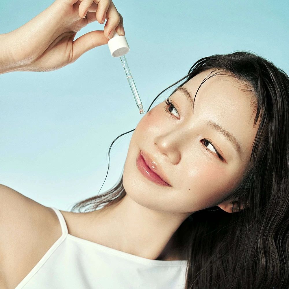 Donna con applicatore di siero. Il siero viene applicato sulla guancia. Sfondo blu.