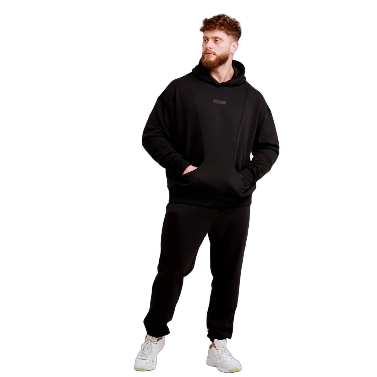 Uomo in pantaloni da jogging neri e felpa con cappuccio, mani nelle tasche.