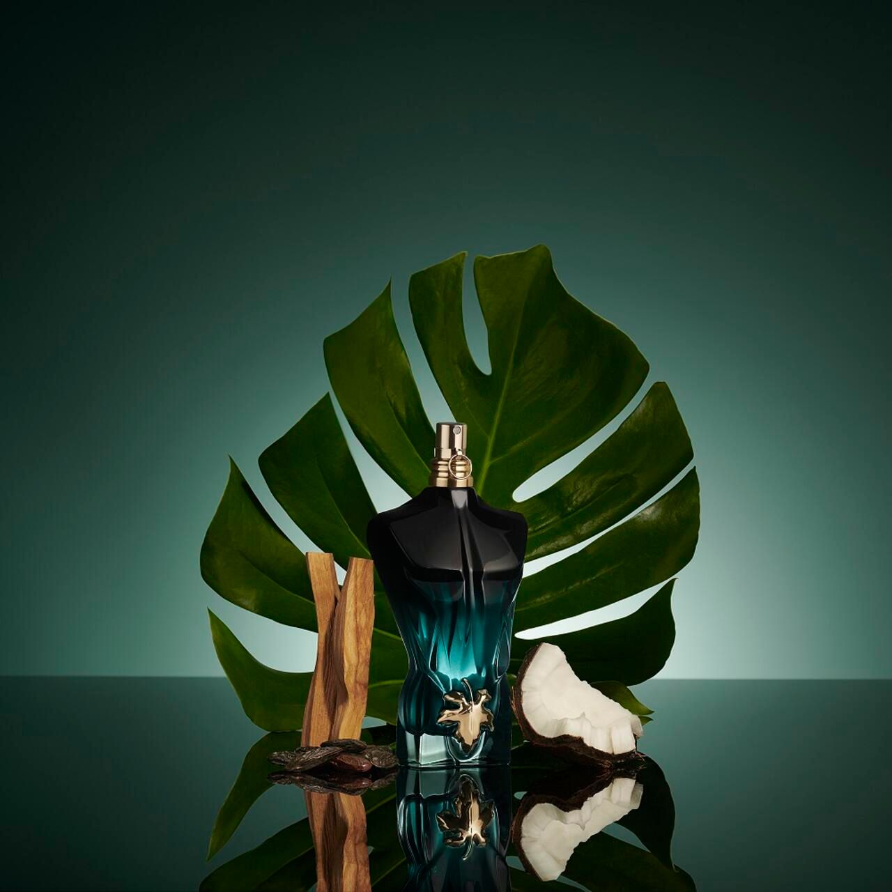 Flacone a forma di busto, accanto a foglia e pezzo di legno. Flacone blu-verde, tappo dorato. Sfondo verde.