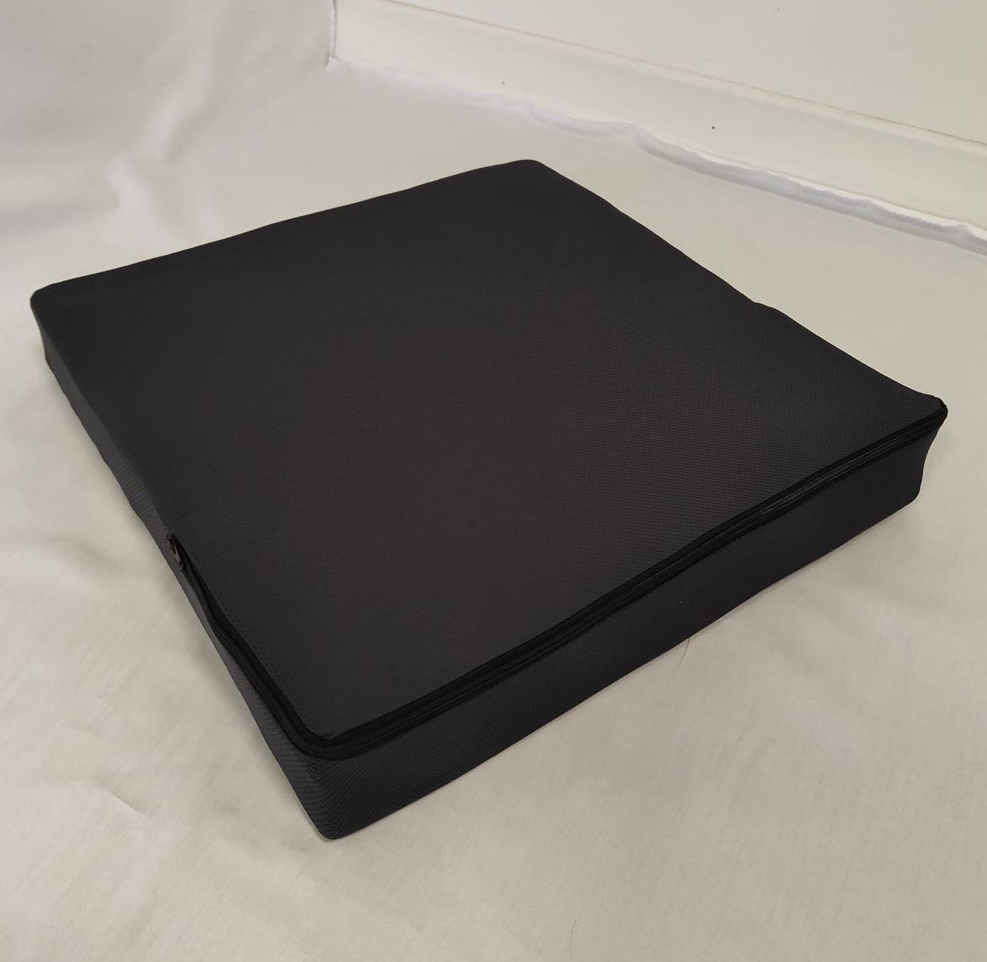 Fodera quadrata per sedile nera con cerniera. La fodera è appoggiata su una superficie bianca.