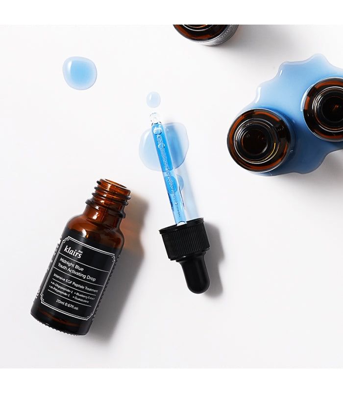 Flacone di vetro marrone con etichetta nera e contagocce. Liquido blu e gocce accanto. Nome del prodotto visibile.