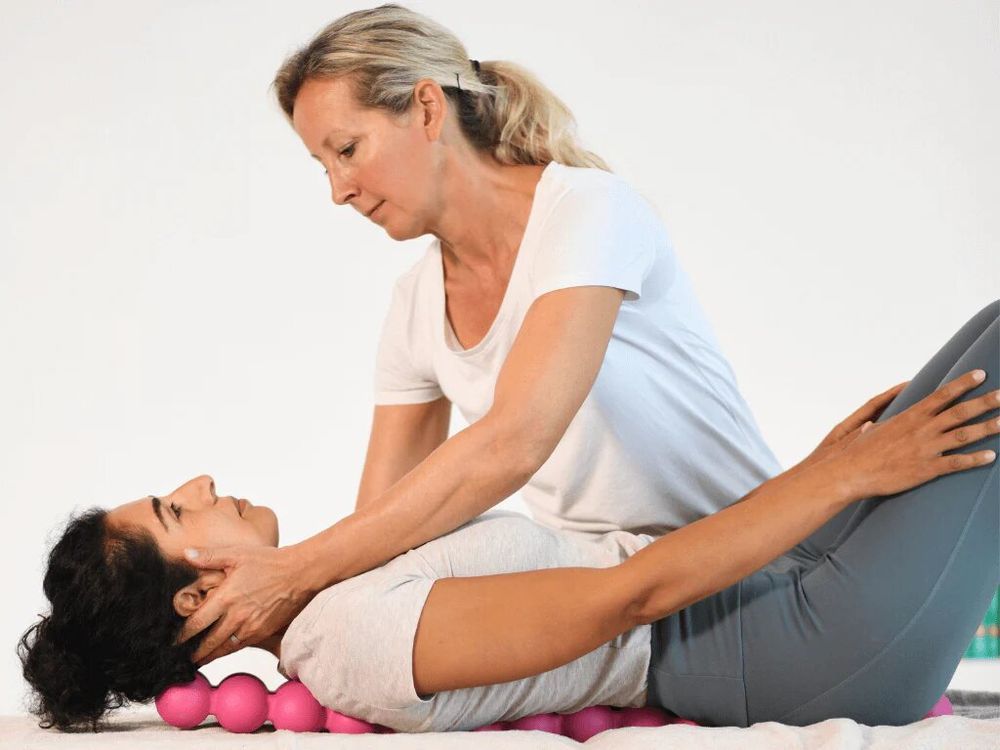 Donna sdraiata sulla schiena, testa su SPINEFITTER® rosa. Un'altra donna le massaggia il collo.