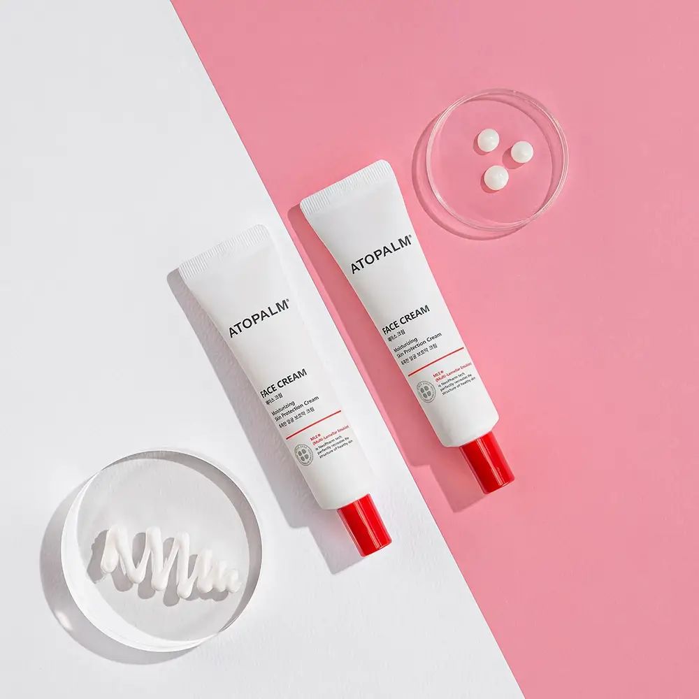 Due tubi con tappo rosso. Scritta ATOPALM FACE CREAM. Su sfondo rosa e bianco.