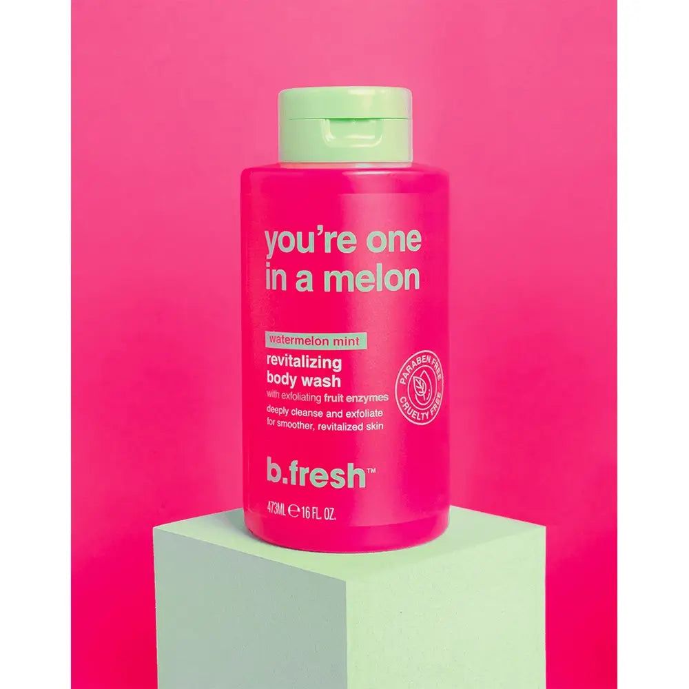 Flacone di gel doccia rosa con tappo verde. Scritta: "you're one in a melon". Marchio: b.fresh. Posizionato su un piedistallo verde.