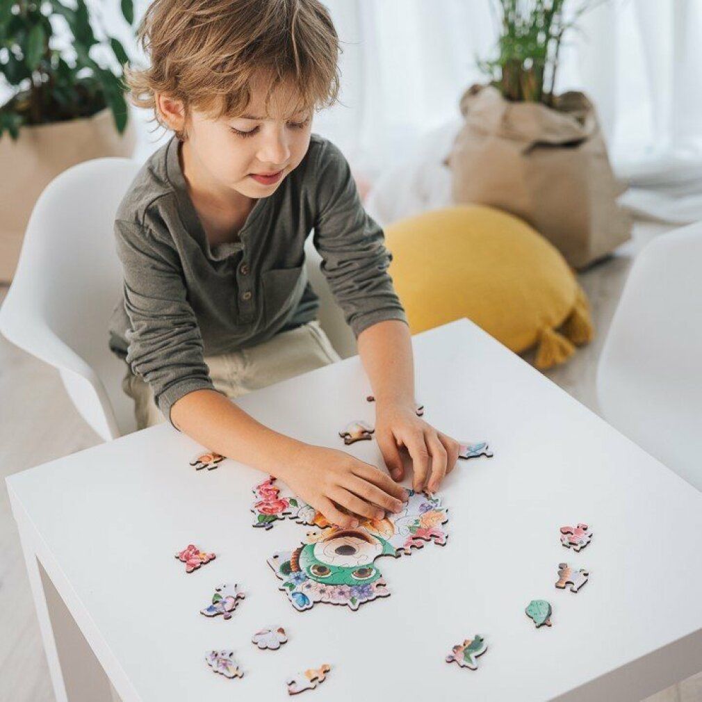 Un ragazzo fa un puzzle su un tavolo. Il puzzle raffigura un orso e un cane. Alcuni pezzi del puzzle sono accanto.