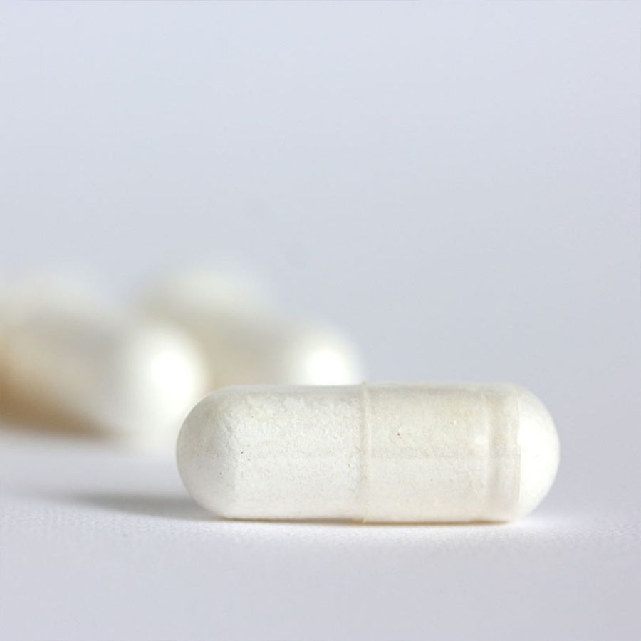 Primo piano di capsule bianche. Capsula singola a fuoco, altre sfocate sullo sfondo. Forma cilindrica liscia.