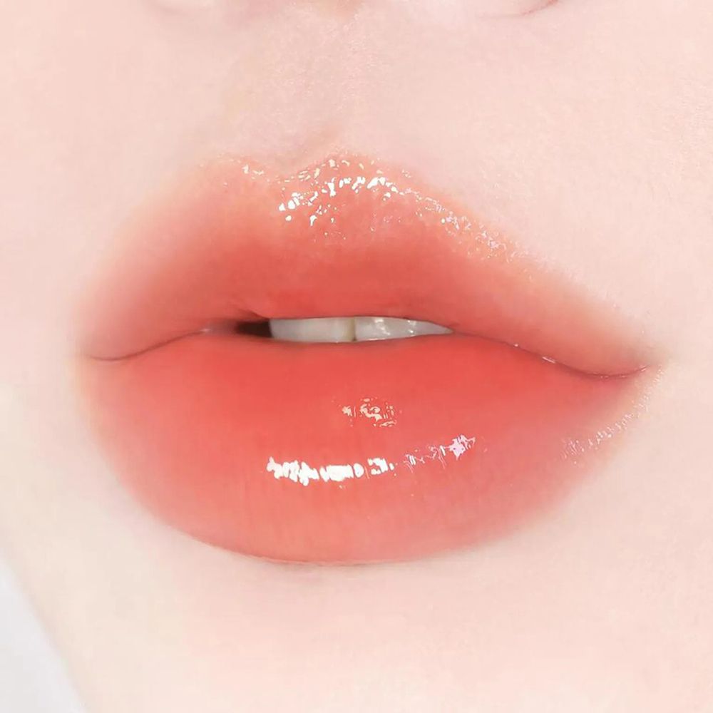 Primo piano di labbra lucide, con balsamo rosa. Le labbra sono leggermente socchiuse.