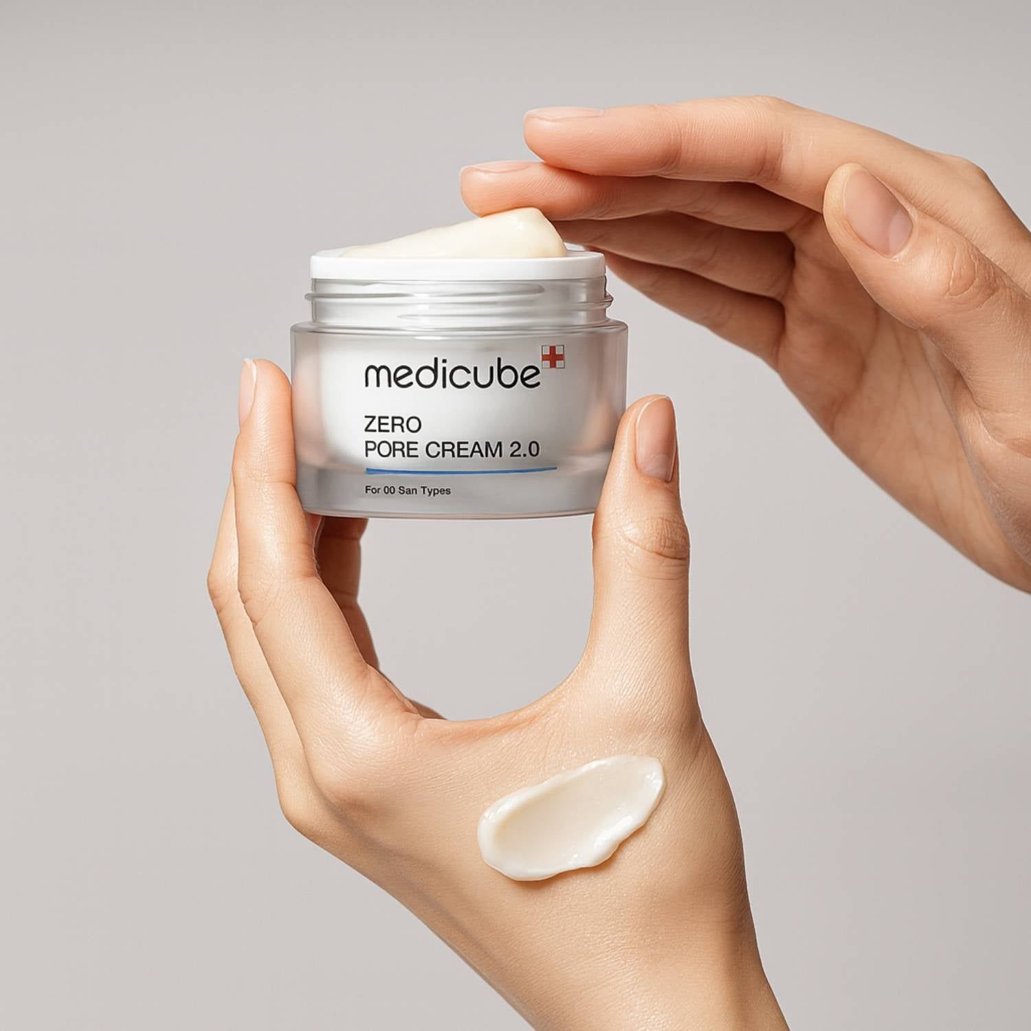 Mani che tengono il vaso MEDICUBE Zero Pore Cream 2.0. Campione di crema sul palmo.