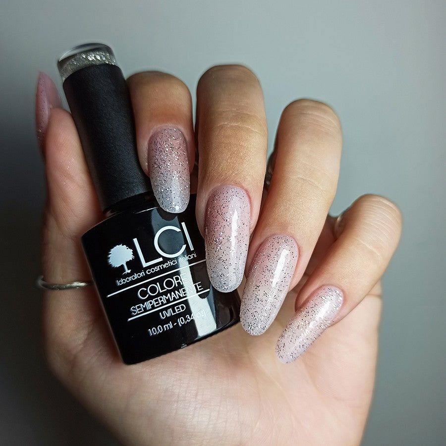 Mano con unghie smaltate e flacone di smalto glitterato argento. Testo: LCI, Colore Semipermanente, UVLED, 10,0 ml.