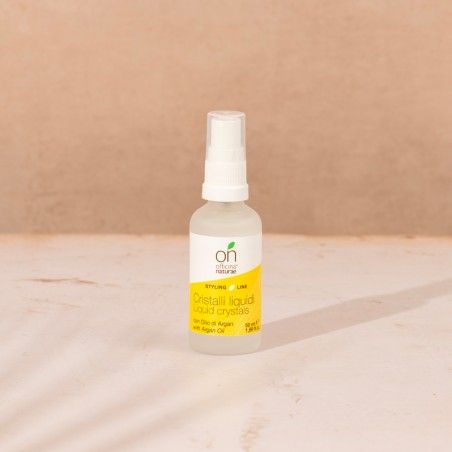 Flacone spray trasparente con tappo bianco. Etichetta gialla con testo: Cristalli liquidi, con olio di Argan. Logo: ON.