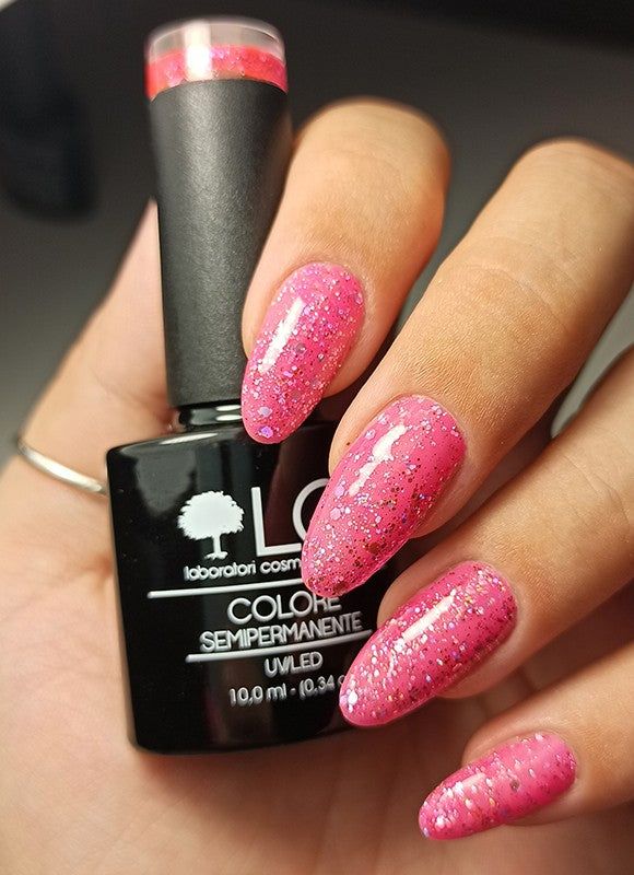 Mano con unghie smaltate rosa con glitter. Flacone di smalto accanto. Scritta: LCI, Colore Semipermanente.