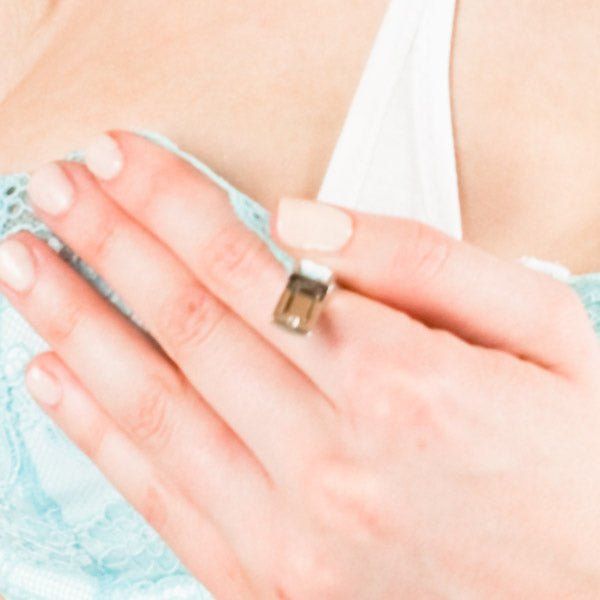 Primo piano di una mano con un anello che tocca una parte di un reggiseno azzurro chiaro. Il reggiseno è in pizzo.