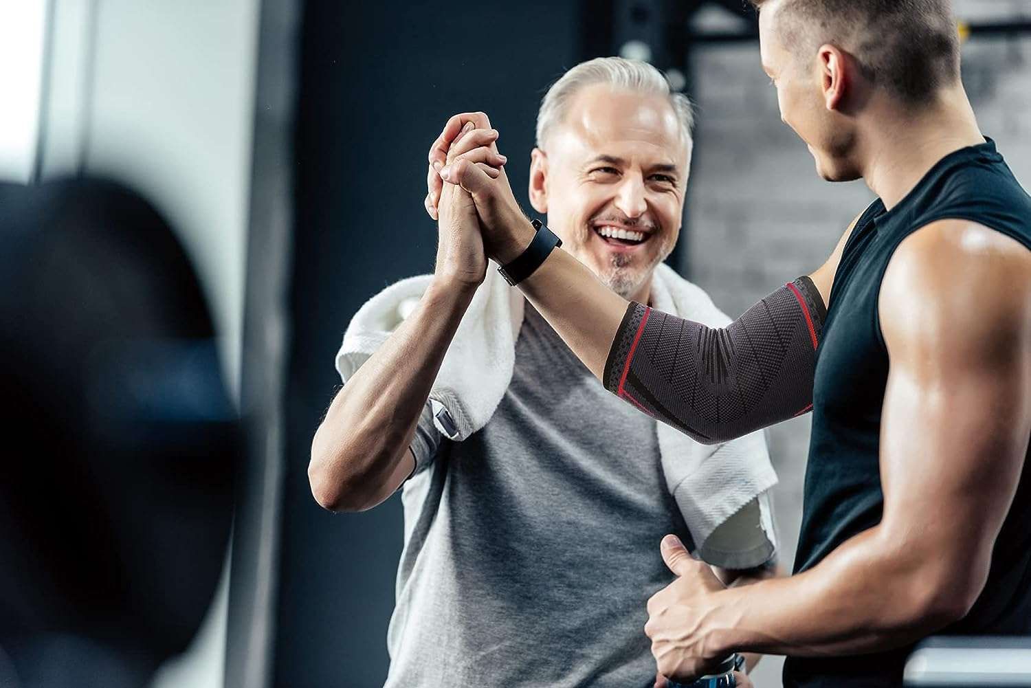 Due uomini in palestra. Uno indossa un tutore per il gomito. Si danno il cinque.