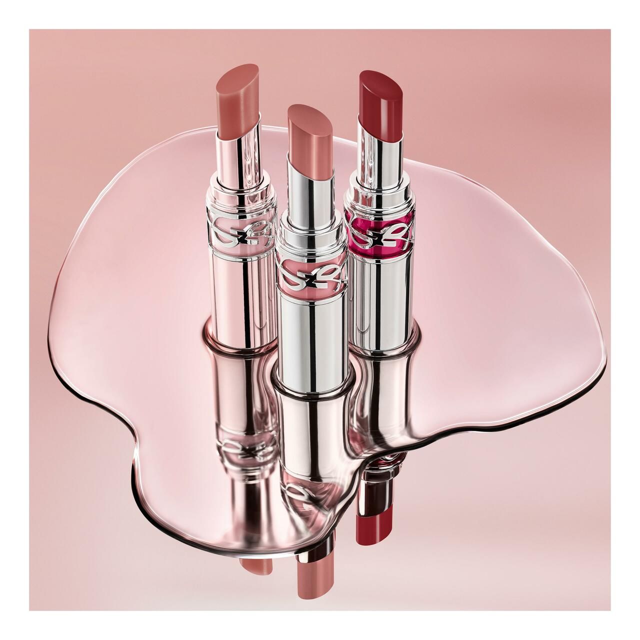 Tre rossetti su una superficie lucida. Tubi argentati con logo rosso. Diverse tonalità di rosso.