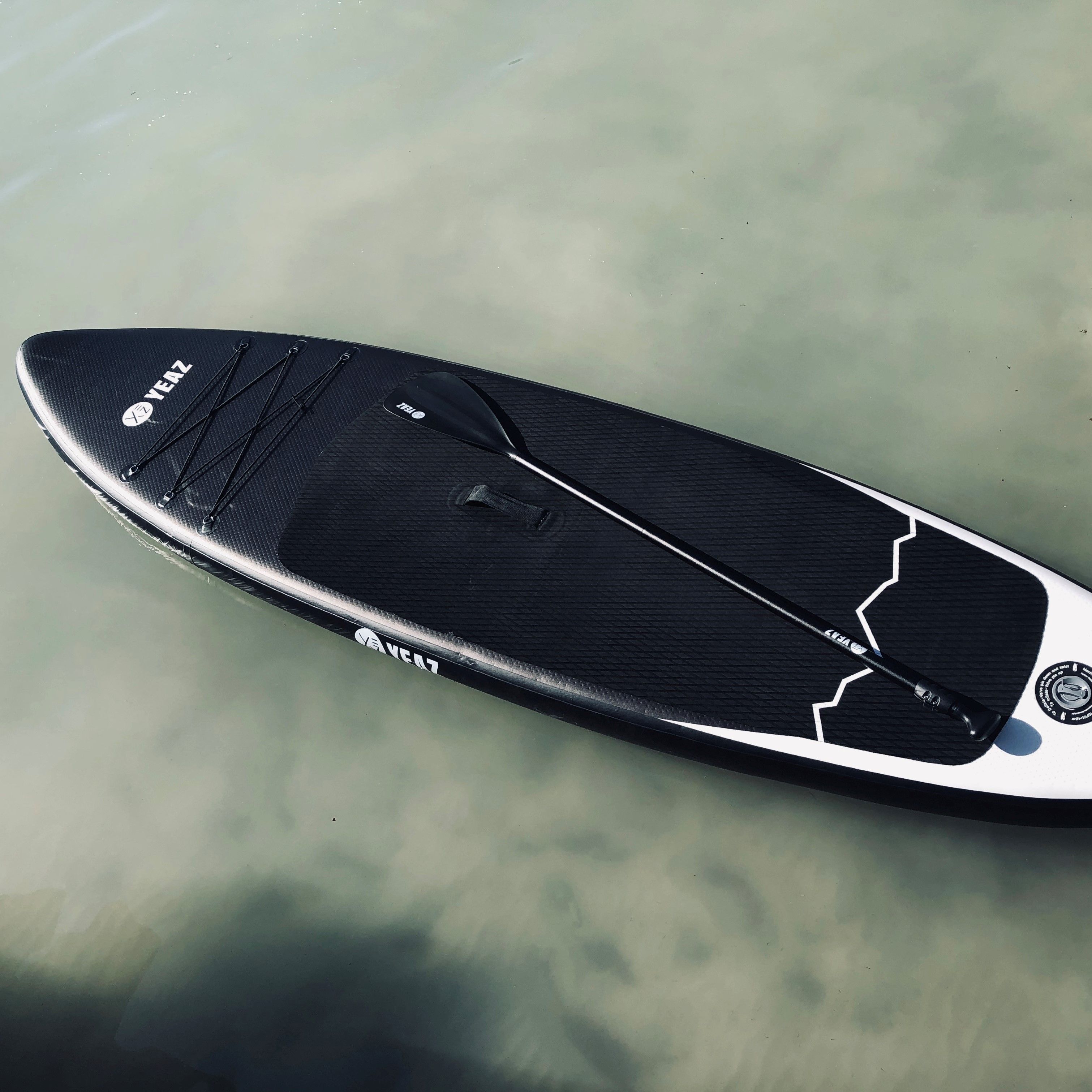 Tavola da Stand-Up Paddle nera con pagaia, marca YEAZ, sull'acqua.
