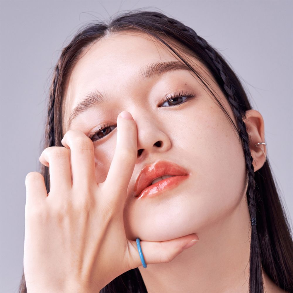 Ritratto di persona con rossetto. Le labbra sono tinte di rosso. La persona tocca il viso con la mano.