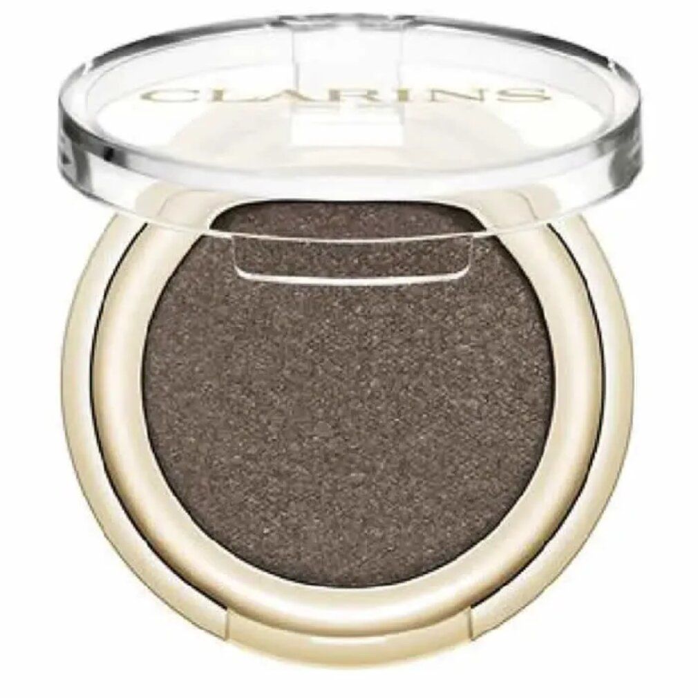 Contenitore rotondo dorato per ombretto con coperchio trasparente. L'ombretto è marrone. Il marchio Clarins è visibile sul coperchio.
