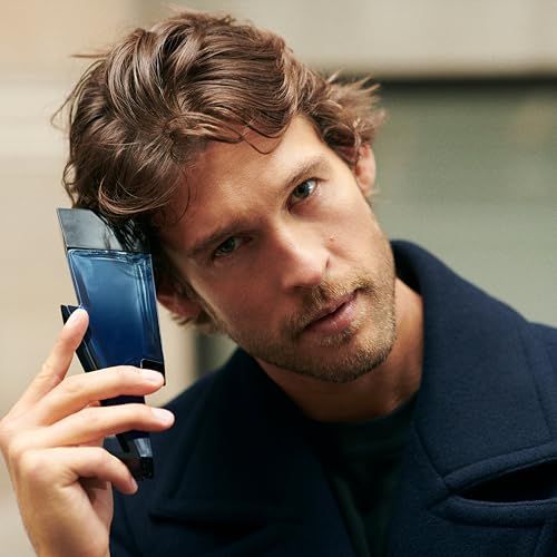 Uomo tiene flacone blu a forma di fulmine. Tappo nero. L'uomo indossa un cappotto.