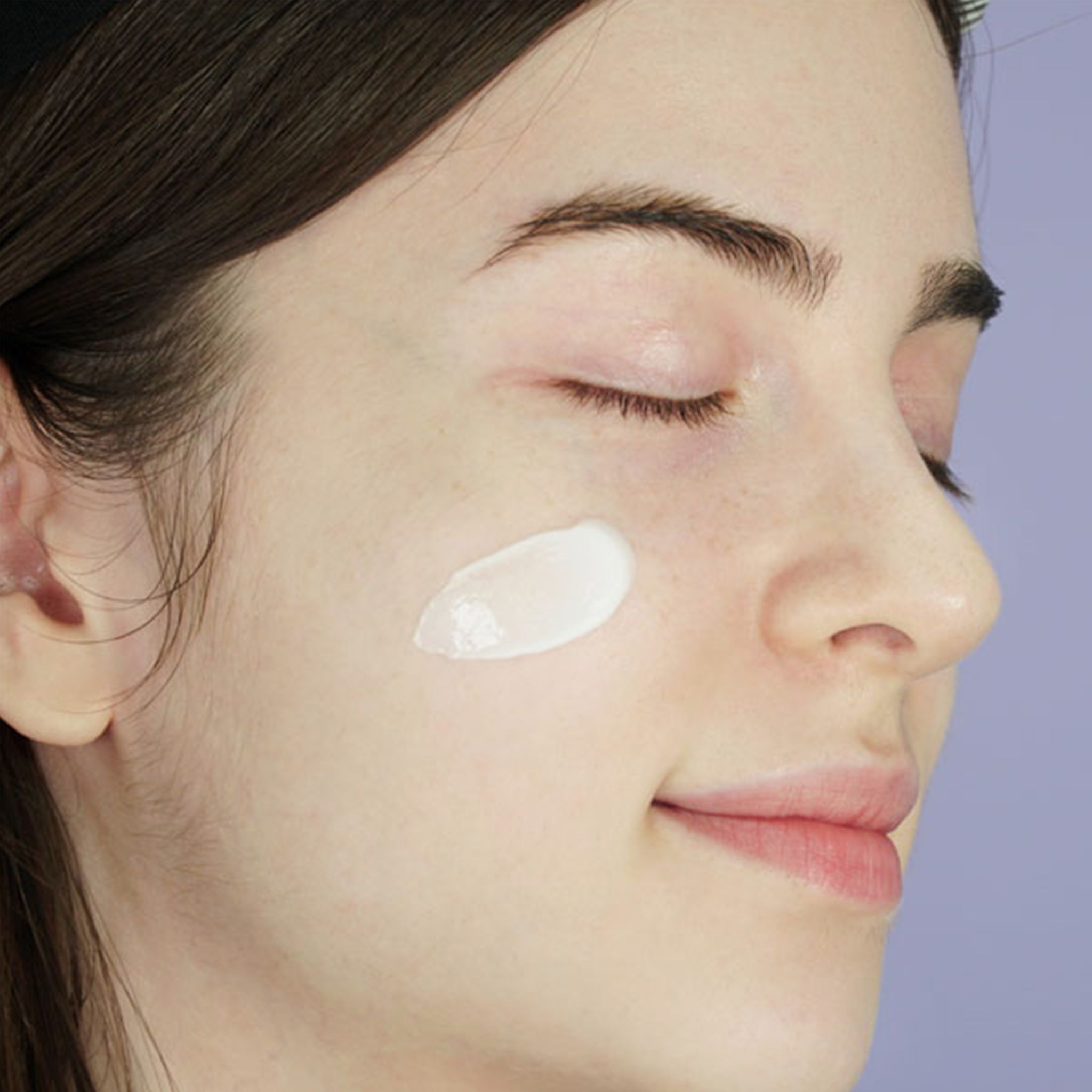 Primo piano di una donna con gli occhi chiusi. Sulla guancia è applicata una crema bianca.