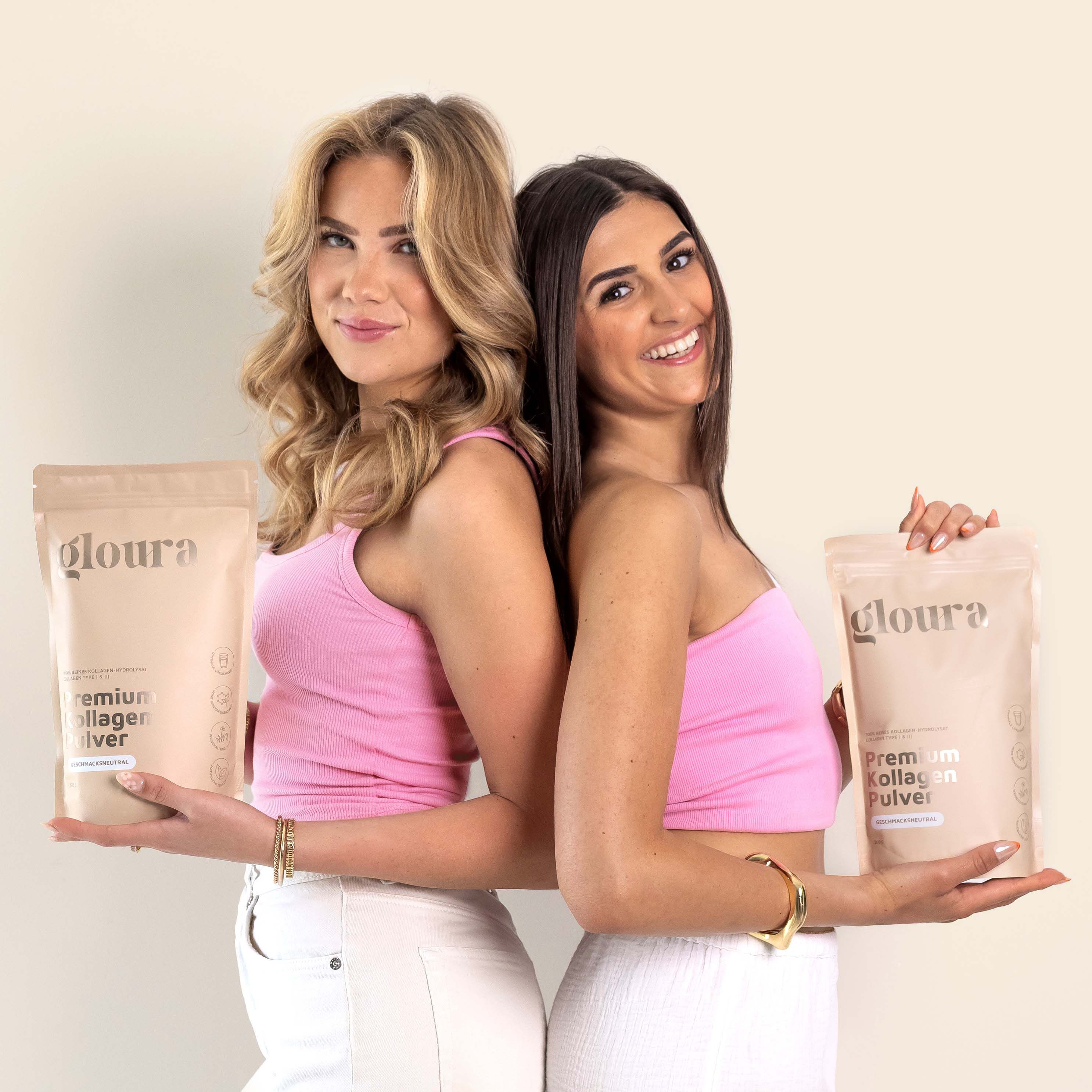 Due donne sono schiena contro schiena e tengono confezioni di Gloura® Kollagen Pulver. Indossano top rosa.