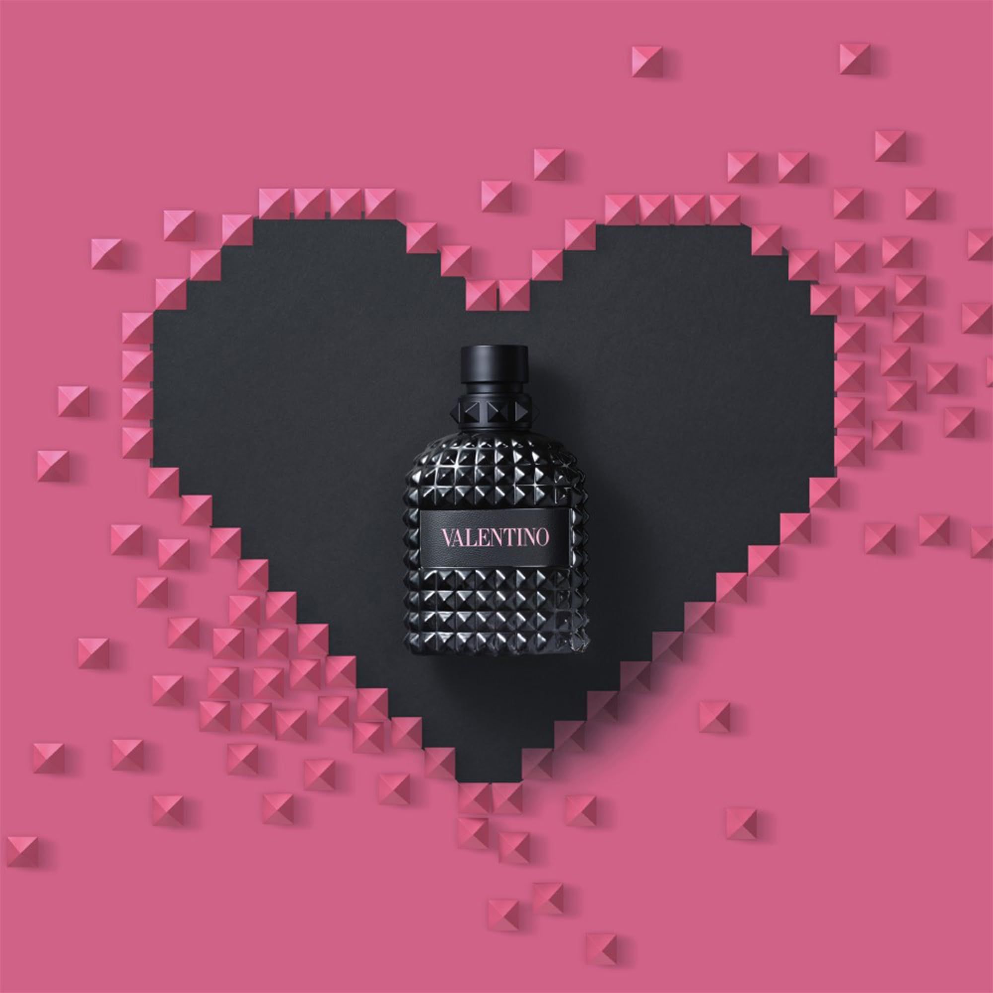 Flacone Valentino su sfondo a cuore nero. Borchie rosa formano un cuore.
