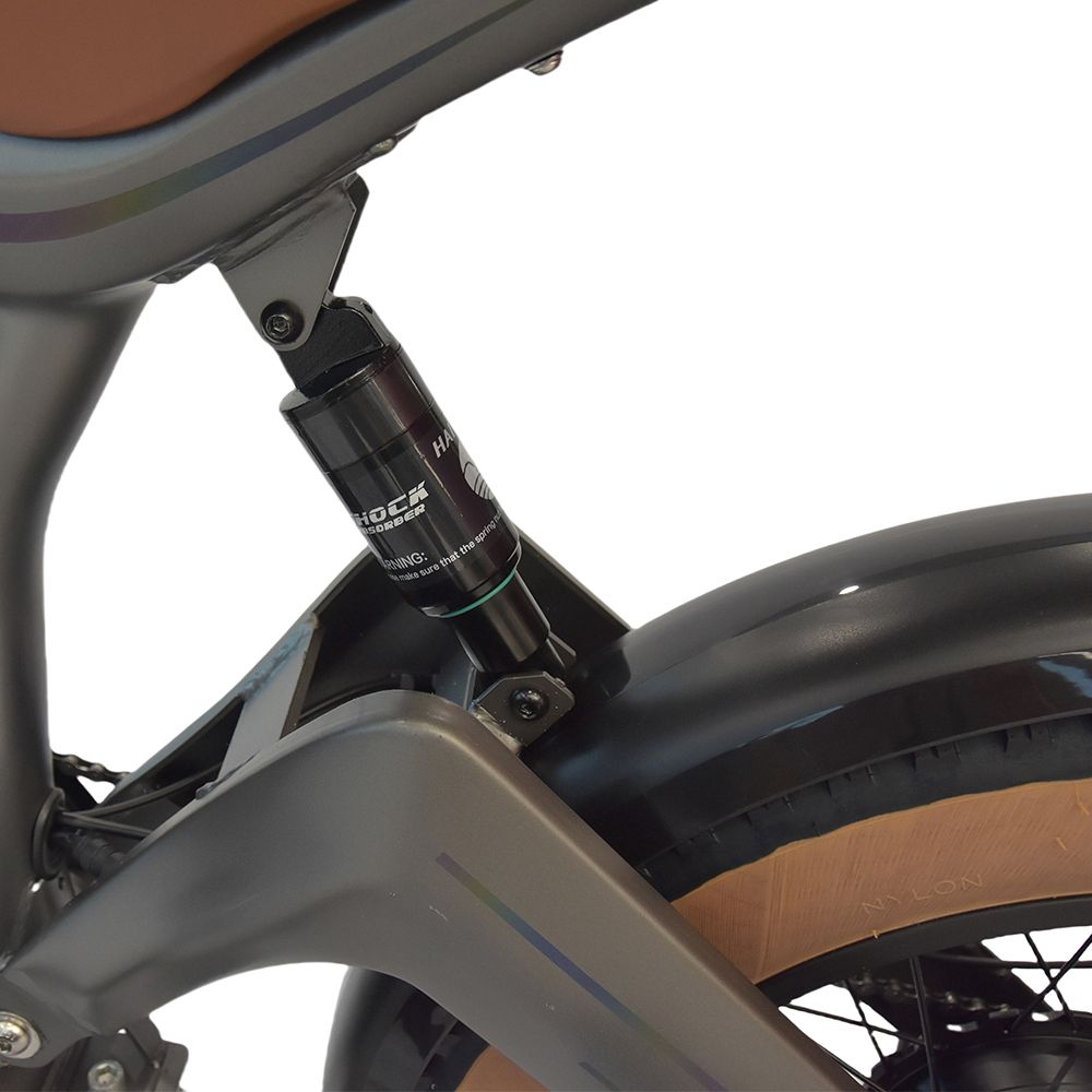 Primo piano dell'ammortizzatore posteriore di una dirt bike elettrica grigia. Dettagli neri e scritta 'SHOCK'.