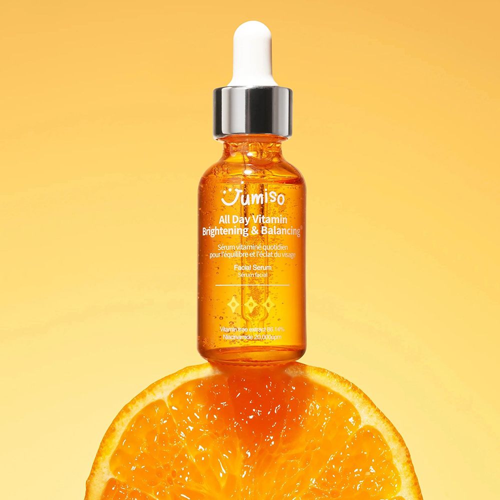 Flacone di siero su una fetta d'arancia. Liquido arancione, tappo argentato. Scritta: JUMISO All Day Vitamin Brightening & Balancing.