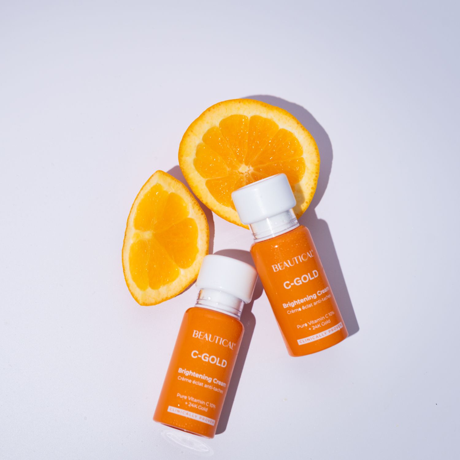 Due flaconi di crema schiarente BEAUTICAL C-GOLD con spicchi d'arancia. Flaconi arancioni con tappo bianco.